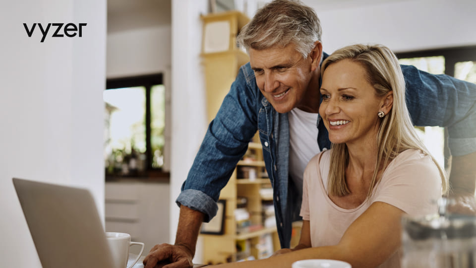 Mature couple smiling while researching wealth management strategies on a laptop at home.