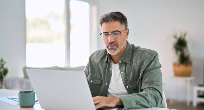 Serious middle-aged man wearing glasses, analyzing private equity dashboards on a laptop while working from home
