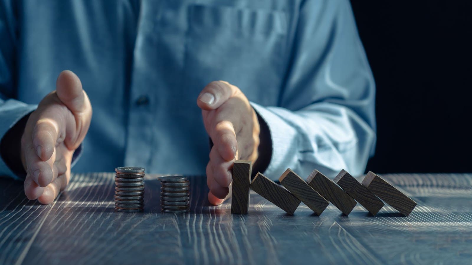 Hands preventing domino crisis effect symbolizing asset protection and financial stability.