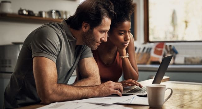Couple with a laptop reviewing financial paperwork, contemplating between good or bad debt.