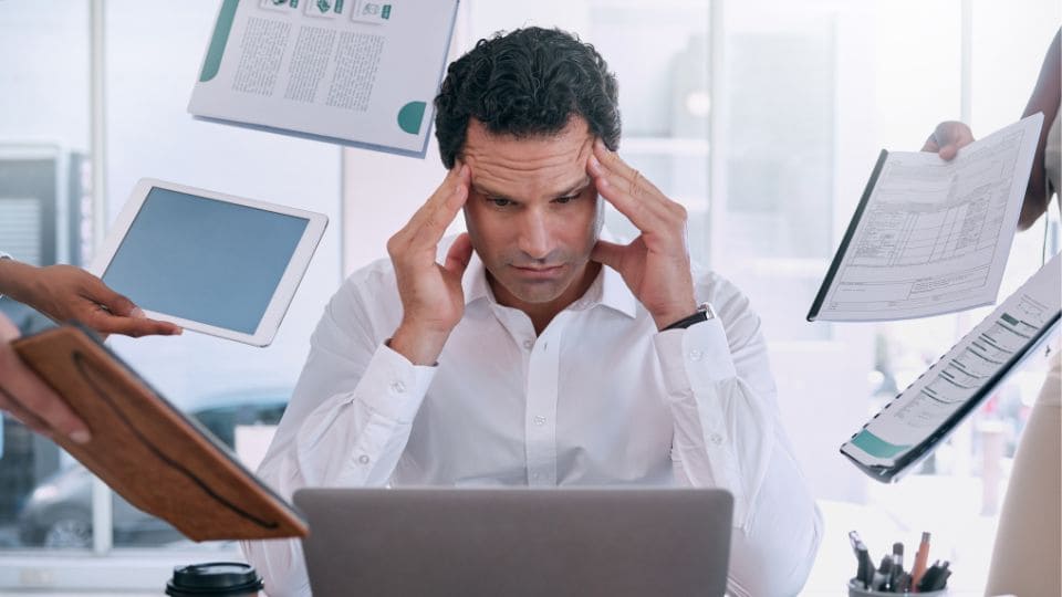 An overwhelmed investor experiencing stress and burnout while juggling multiple financial tasks on a laptop, indicating the challenges of managing diversified income sources